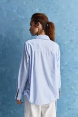 Camisa celeste de calce relajado, con cuello camisero, bolsillo aplicado en el pecho y mangas largas con puños abotonados. Cuenta con lazos ajustables en los laterales para fruncir y regular la silueta.