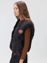 Chaleco de corte cuadrado con diseño bicolor en tonos terracota y crema. Presenta cierre frontal metalizado, parches de nylon en el pecho, interior forrado en corderito y cordón ajustable en el ruedo.