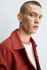 Cazadora de algodón color terracota, de corte cropped y calce holgado. Presenta cuello solapa, manga larga con puño abotonado, dos bolsillos de vivo en el pecho y bolsillos laterales en la cadera. Cierre frontal con botonadura oculta.