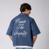 Camisa de manga corta azul oscuro de corte boxy, confeccionada en algodón. Presenta cuello camisero, cierre frontal con botones y un pequeño bordado en el pecho con las siglas 'VCP CNPT' y el número '333'.