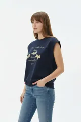Musculosa color crudo con estampado frontal de paisaje montañoso y texto "EXPLORING Outlands", corte holgado y aberturas laterales en el ruedo.