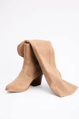 Bota de caña alta confeccionada en cuero vacuno, con diseño versátil que permite doblar la caña. Presenta un taco cuadrado de altura media y punta redondeada.