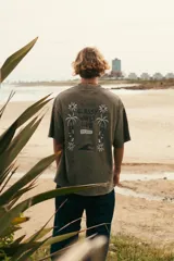 Remeron de algodón color verde musgo con efecto lavado, de manga corta y corte oversize. Presenta una estampa en la espalda con diseño inspirado en la playa, palmeras y flores, junto con la inscripción "Glassy Waves Club".