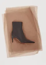 Botín de cuero caprino color marrón oscuro, con diseño de punta fina y tacón kitten de 6,5 cm. Presenta cierre de cremallera lateral.