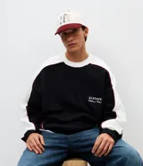 Buzo de corte boxy con diseño color block en negro, blanco y detalles en bordó. Presenta cuello redondo, mangas largas con puños acanalados y estampado lettering frontal con la frase Elevate Clothing & Culture.