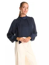 Blusa satinada de cuello alto con frunces, detalle de lazo lateral y cierre de botones. Presenta mangas largas estilo balloon con puños ajustados.