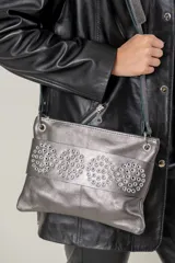 Sobre de cuero vacuno color bordó, con diseño frontal decorado con múltiples remaches metálicos circulares. Cuenta con correa larga ajustable y extraíble, cierre superior y bolsillo trasero con cierre.