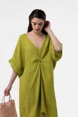 Vestido midi de lino color marrón, de corte amplio y silueta asimétrica con escote en V y detalle fruncido en el centro del frente. Presenta mangas cortas holgadas con vuelta y diseño relajado.