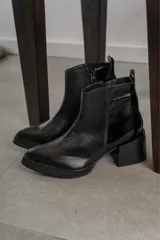 Bota corta de cuero negro con acabado combinado mate y charol. Presenta una tira decorativa con tachas metálicas y hebilla en el tobillo, tacón cuadrado robusto y suela con plataforma.