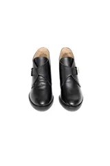 Bota corta de cuero vacuno grabado con terminación charolada, color negro. Presenta un diseño de solapa cruzada con cierre de hebilla metálica plateada y taco medio fachetado con efecto madera.