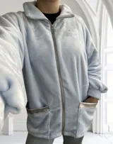 Campera celeste de tela tipo peluche, con cierre frontal, cuello alto y bolsillos con ribete plateado.