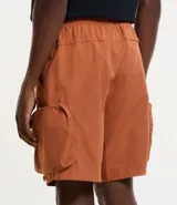 Bermuda cargo color terracota con cintura elástica y cordón de ajuste. Presenta múltiples bolsillos tácticos laterales con cierre y recortes decorativos.