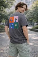 Remera manga corta color gris oscuro con un estampado gráfico en la espalda dividido en cuatro paneles: una luna creciente naranja, una figura humana sosteniendo un objeto en un fondo rosa, otra figura humana sosteniendo un objeto en un fondo azul, y una flor estilizada en un fondo verde.