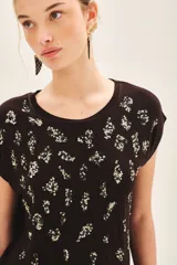 Remera de viscosa negra de calce suelto con escote redondo y manga corta. Presenta un estampado frontal centrado de pequeños motivos florales o abstractos en lentejuelas doradas o plateadas.