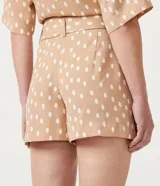 Short color beige con estampado de lunares blancos, tiro medio, trabillas en la cintura y cinturón forrado con hebilla.