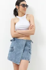 Minifalda de jean celeste con corte asimétrico, bolsillos de parche con solapa y tiras ajustables con hebillas en los laterales.