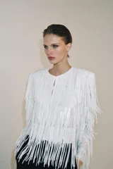 Chaqueta de cuello redondo y manga larga con hombreras, completamente cubierta de flecos con lentejuelas. Cuenta con forro interior y cierre frontal.
