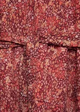 Vestido corto de tejido fluido con estampado floral en tonos rojizos. Presenta cuello redondo con cierre de botones frontal, mangas largas con puños elásticos y lazo ajustable en la cintura. Diseño evasé con forro interior.