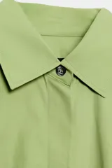 Camisa oversize verde de popelina de algodón, con cuello solapa, manga larga y cierre frontal con botones ocultos bajo solapa.