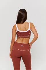 Conjunto deportivo de dos piezas color chocolate con detalles de costuras blancas. Incluye un top de tirantes finos con escote redondo y un pantalón largo de corte ajustado con aberturas en el bajo.