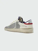 Zapatillas Golden Goose modelo Stardan con diseño tricolor. Presentan cuerpo de cuero blanco con paneles laterales de malla gris, estrella lateral de gamuza roja, puntera de gamuza gris y detalles en azul marino en el talón. Incluyen suela con efecto desgastado característico de la marca.