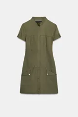 Vestido corto de estilo utilitario en color verde militar, confeccionado en gabardina. Presenta cuello redondo, cierre frontal con cremallera oculta, mangas cortas con detalle de trabilla y botón, y bolsillos de plastrón en el frente.