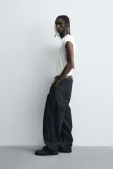 Jeans de denim oscuro, corte ancho (baggy fit) y tiro medio, con costura central girada en el frente de ambas piernas. Presenta pespuntes en color caramelo.