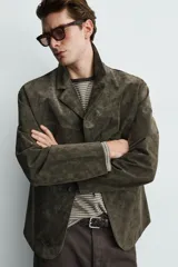 Blazer de corte relajado confeccionada en piel con acabado de ante. Presenta cuello con solapas de muesca, cierre frontal de tres botones y bolsillos de doble vivo en la cadera.