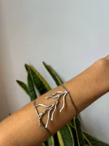 Brazalete plateado rígido con diseño de ramita.