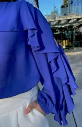 Blusa azul con escote redondo, mangas largas con aberturas en los hombros y volados en los brazos.