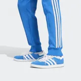 Pantalón deportivo azul con corte ajustado, cintura elástica con cordón ajustable, bolsillos frontales, puños de canalé y escudo del Real Madrid bordado.