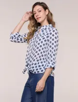 Camisa de gasa blanca con estampado de lunares en tonos azules, cuello con solapa, cierre frontal de botones, bolsillo aplicado en el pecho y detalle de nudo en el dobladillo inferior. Cuenta con mangas largas regulables.