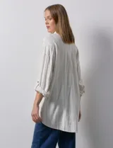 Camisa de lino a rayas verticales color crema, con cuello con solapa, abertura central con botones, bolsillos delanteros y mangas 3/4 regulables con presilla y botón.