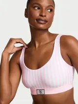 Bralette sin aros color blanco con rayas rosadas, escote redondo y copas ligeramente acolchadas. Cuenta con una banda elástica rosada con un parche brillante con el logo en pedrería en el centro.