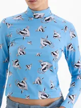 Top de cuello polera y mangas largas, confeccionado en tela de punto con estampado de corazones atravesados por flechas sobre fondo azul. Presenta un diseño ajustado al cuerpo.