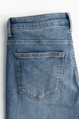 Pantalón jean acampanado de tiro bajo en denim levemente elástico, con bolsillos delanteros decorativos, bolsillo monedero y bolsillos abiertos atrás.
