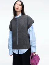 Chaleco de tejido de punto color gris, con cuello redondo y cierre frontal completo a contratono en color celeste. Presenta un diseño sin mangas con terminaciones acanaladas en cuello, sisas y ruedo.