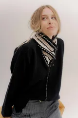 Polera tejida en lambswool color negro, con cuello alto y diseño de intarsia en blanco y beige. Presenta botones forrados en el frente para modular la apertura.