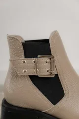 Botineta de cuero charol negro con acabado brillante, diseño de punta fina y taco cuadrado. Presenta un panel elástico lateral y una correa decorativa con hebilla metálica plateada.