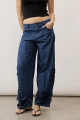 Jean de corte cargo y estilo holgado, con diseño de rayas verticales en tonos de azul. Presenta bolsillos laterales con solapa y detalles de tiras ajustables con hebillas en los tobillos.