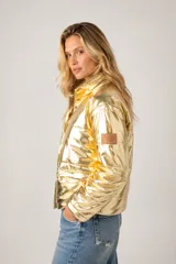 Campera puffer de diseño metalizado en color dorado, con cuello alto, cierre frontal y parche de cuero con logo en la manga.