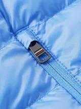 Chaleco acolchado celeste con capucha desmontable, cierre frontal con cremallera y dos bolsillos laterales con cremallera. Logo de Tommy Hilfiger bordado en el pecho.