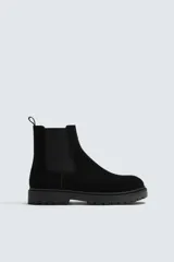 Bota tipo Chelsea de hombre con acabado en serraje, elásticos laterales y tirador trasero. Presenta horma redonda y suela track con volumen.