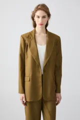 Blazer sastrero color verde oliva, de solapa amplia y fit recto. Cuenta con acceso por botón central, bolsillos delanteros, hombreras y forro completo.