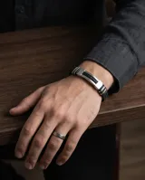 Pulsera masculina de diseño moderno, combinando eslabones de acero inoxidable con una banda central de goma negra trenzada. Cuenta con un cierre de seguridad metálico integrado.