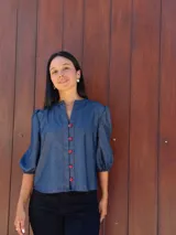 Camisa de jean azul con cuello mao, cierre frontal con botones rojos y mangas tres cuartos abullonadas con puños elásticos.