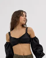 Top negro corto con diseño off-the-shoulder y tirantes, mangas abullonadas caídas con puños elásticos y detalle fruncido en el centro del busto.