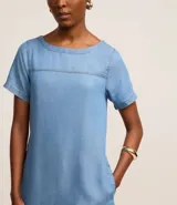 Vestido corto de color azul claro, confeccionado en liocel, con cuello redondo, mangas cortas y detalle de costura horizontal en el busto. Cuenta con bolsillos laterales.