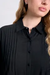 Vestido camisero corto negro, de manga tres cuartos, con cuello camisero y detalle de tablas verticales en el frente. Presenta bolsillos laterales y un calce holgado.