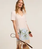 Vestido corto de corte recto y escote en V, color beige claro con estampado de paisaje tropical con palmeras en la parte inferior, mangas cortas y bolsillos laterales. Marca Marfinno.
